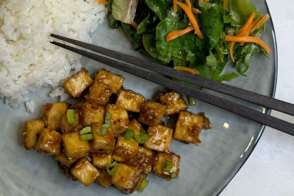 Honey sesame tofu on a plate with rice and salad